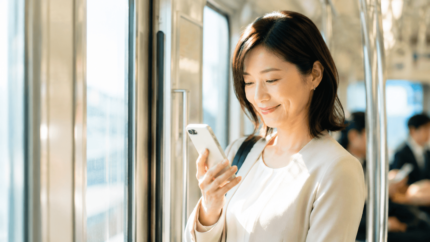 40代の女性が電車の中でスマートフォンの通知を見て微笑んでいる